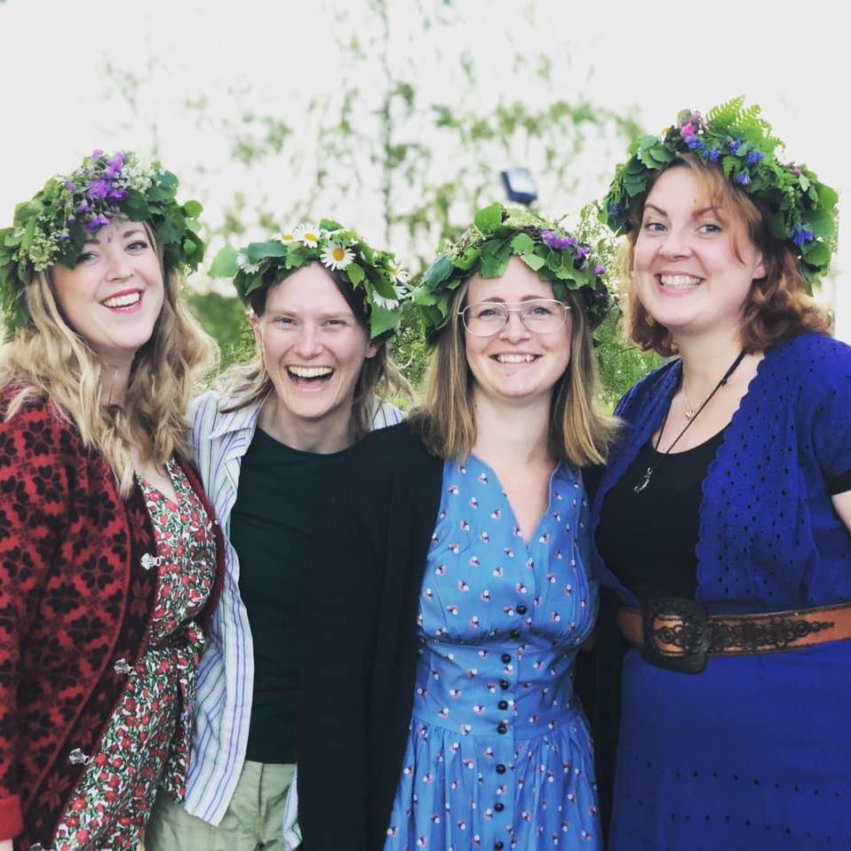 Fyra personer som har midsommarkransar på huvudet och är glada